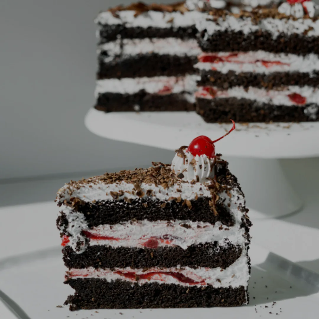 A slice of Black Forest cake with a cherry, beside the cake on its stand